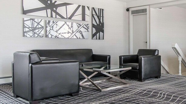 A modern room with a black leather sofa, a glass coffee table, and abstract wall art. - Econo Lodge (Temiskaming Shores)