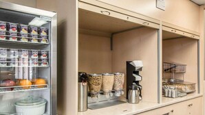 A self-service breakfast area with a refrigerated display case, coffee machine, and various food containers. - Econo Lodge (Temiskaming Shores)
