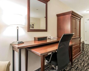 A hotel room with a wooden desk, a black office chair, a telephone, a lamp, and a wardrobe. - Econo Lodge (Temiskaming Shores)