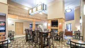 A hotel lobby with a large dining area, a TV mounted on a wooden wall, and a patterned carpet. - Quality Inn & Suites Casper near Event Center (Casper)