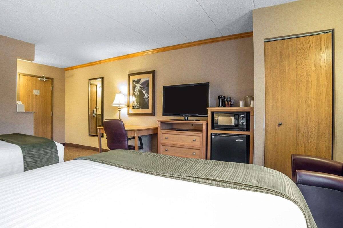 A hotel room with a bed, a desk with a television, a microwave, and a refrigerator.