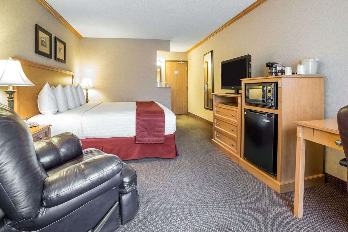 A hotel room with a bed, a desk, a TV, a microwave, and a refrigerator.