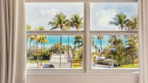 A view through a window with three panes, overlooking a beach with palm trees and a clear sky. - Lorraine Hotel (Miami Beach)