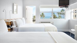 A hotel room with two beds, a desk with a telephone, a TV, and a window with a view of palm trees and the ocean. - Lorraine Hotel (Miami Beach)