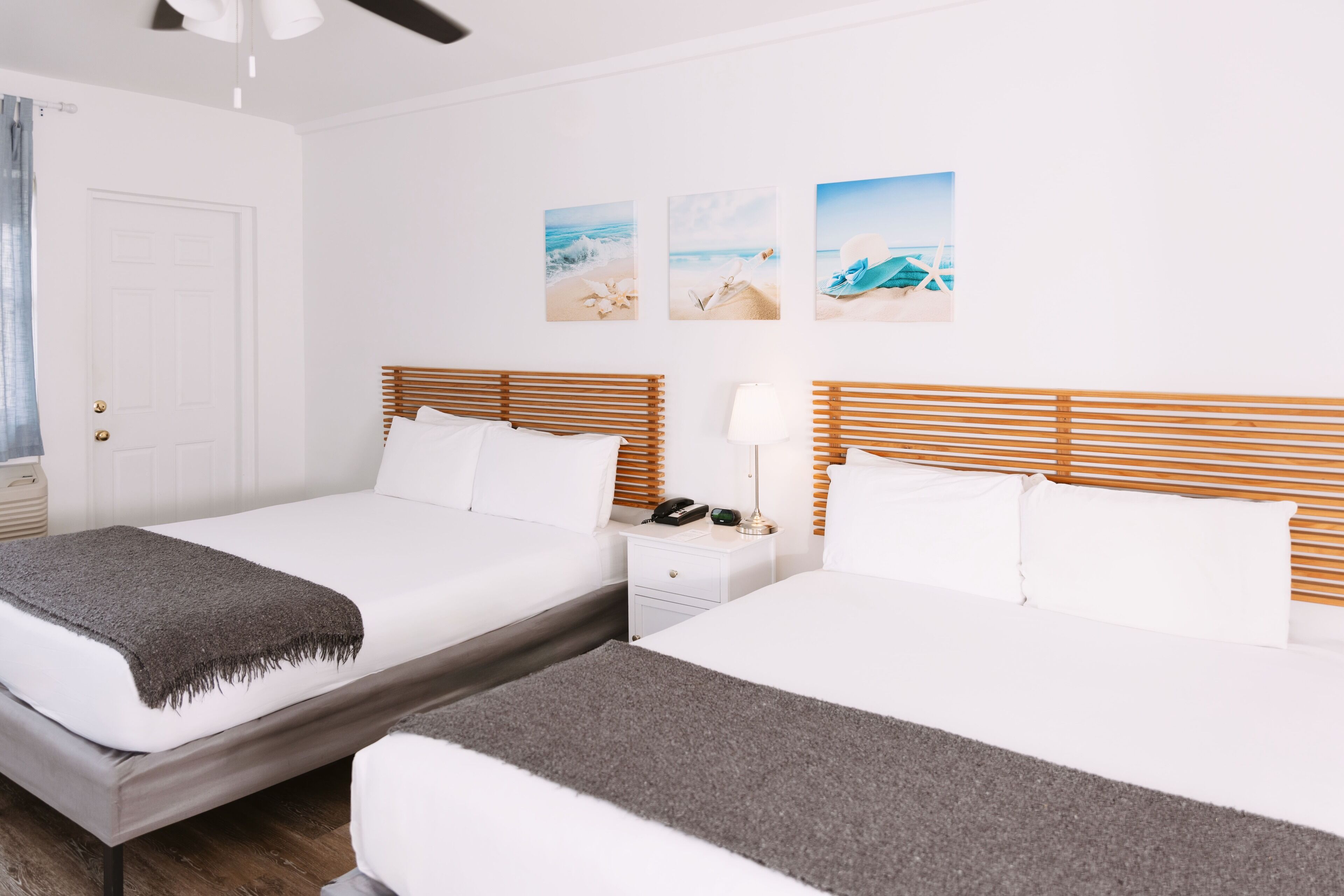 Een hotelkamer met twee bedden, een nachtkastje met een lamp en wanddecoraties met strandtaferelen.