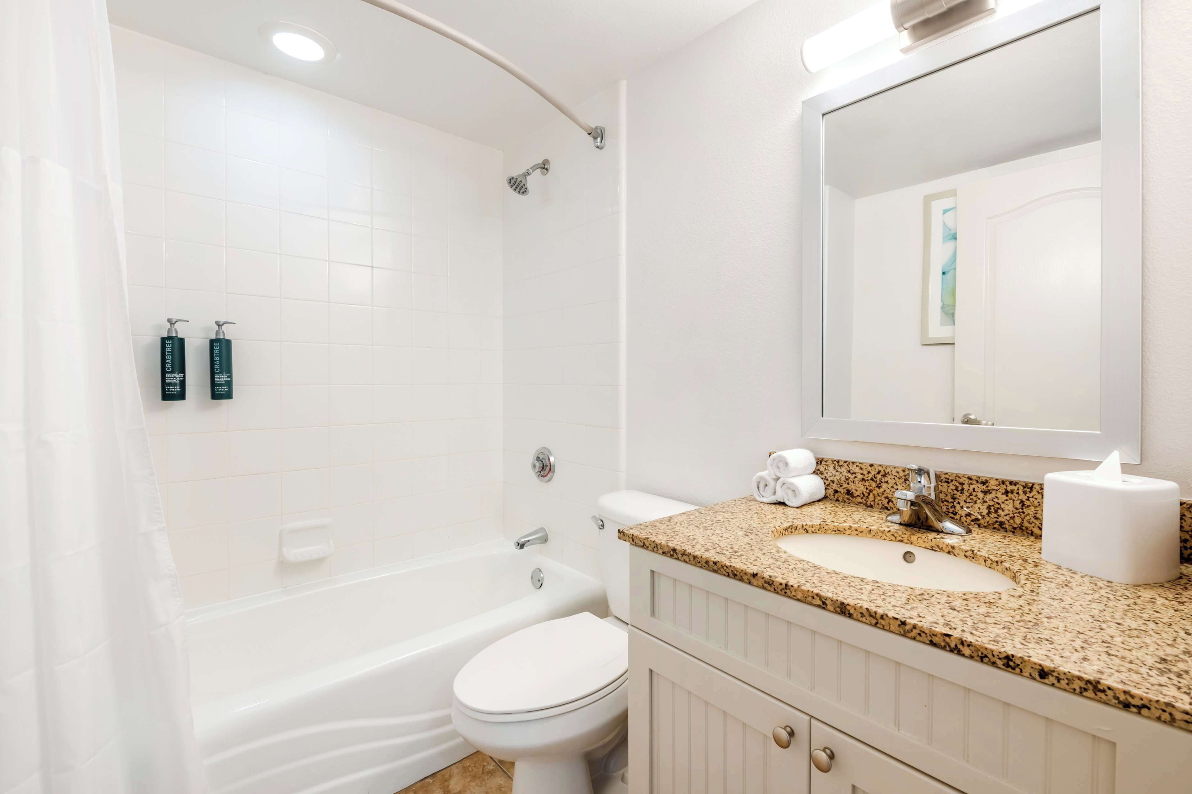 A bathroom with a white bathtub, toilet, and sink. There are two bottles of lotion on the wall, a towel on the sink, and a mirror above the sink.