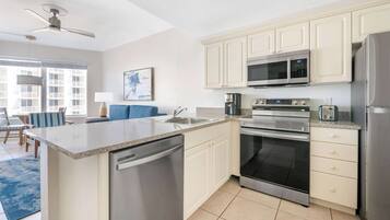 A modern kitchen with a dishwasher, microwave, oven, and refrigerator. There is a dining area with a blue sofa and a coffee maker.