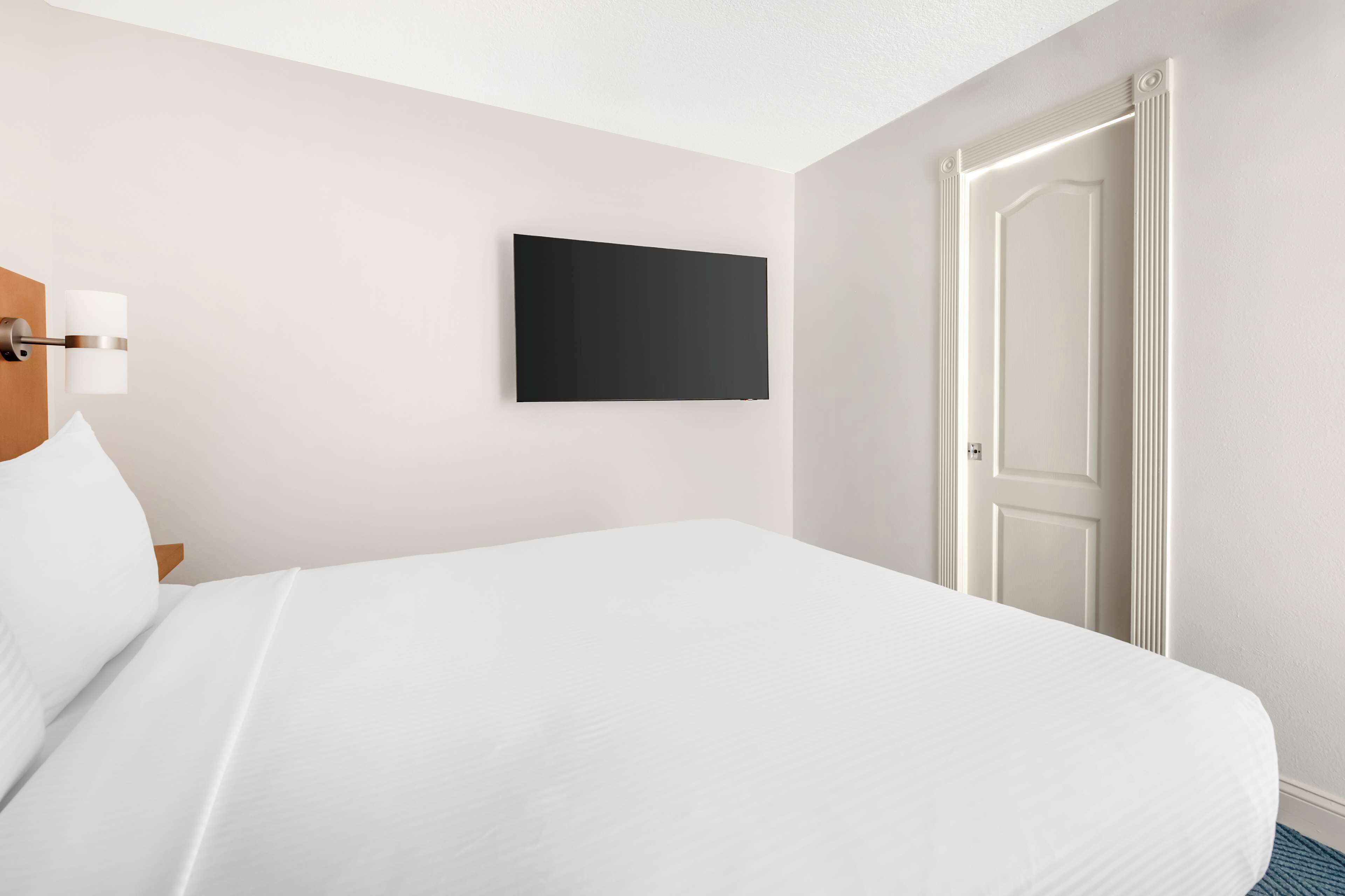 A hotel room with a bed, a flat-screen TV mounted on the wall, and a door.