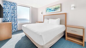 Une chambre d’hôtel avec un grand lit, une table de chevet, une commode, une télévision et une fenêtre avec des rideaux.