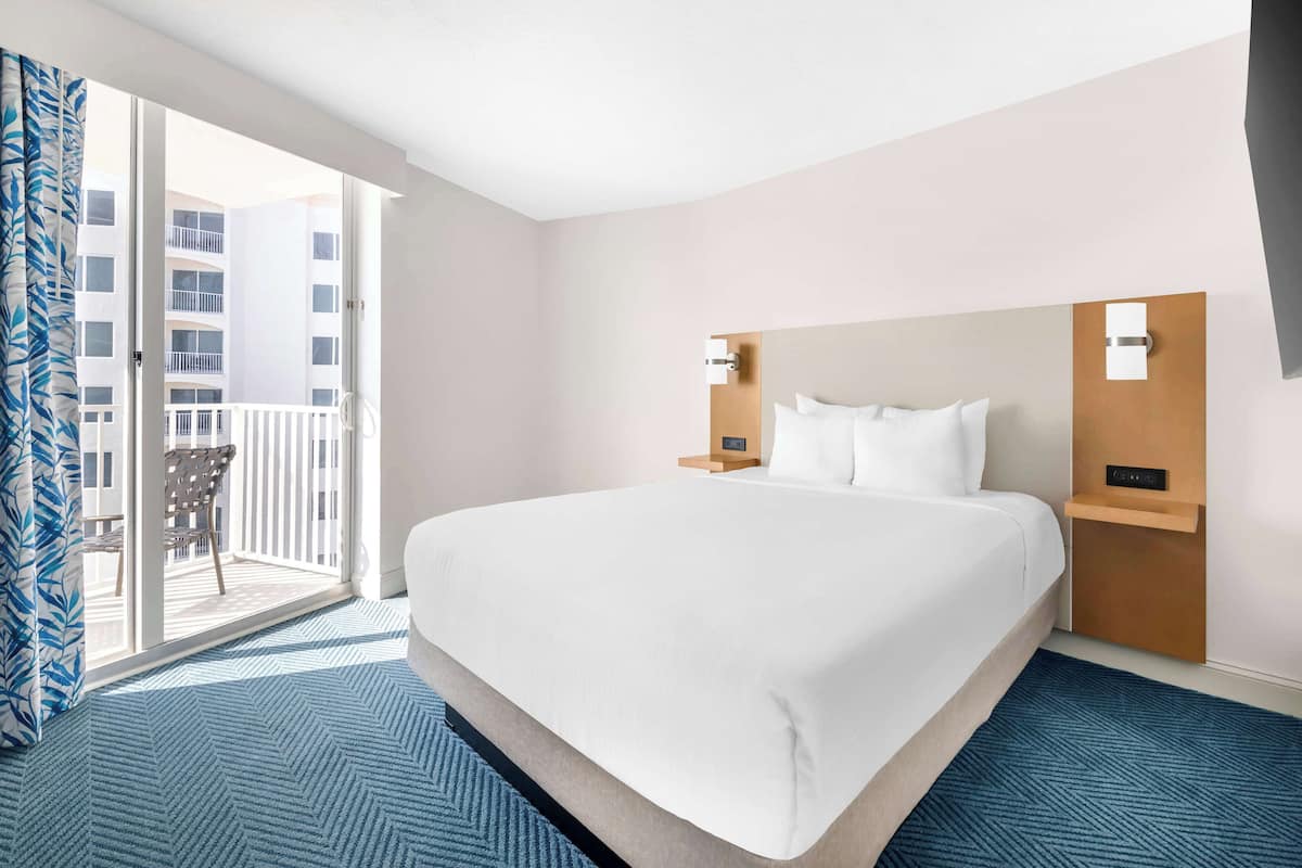 Ein Hotelzimmer mit einem großen Bett, einem Nachttisch, einer Wandlampe und Blick auf einen Balkon.