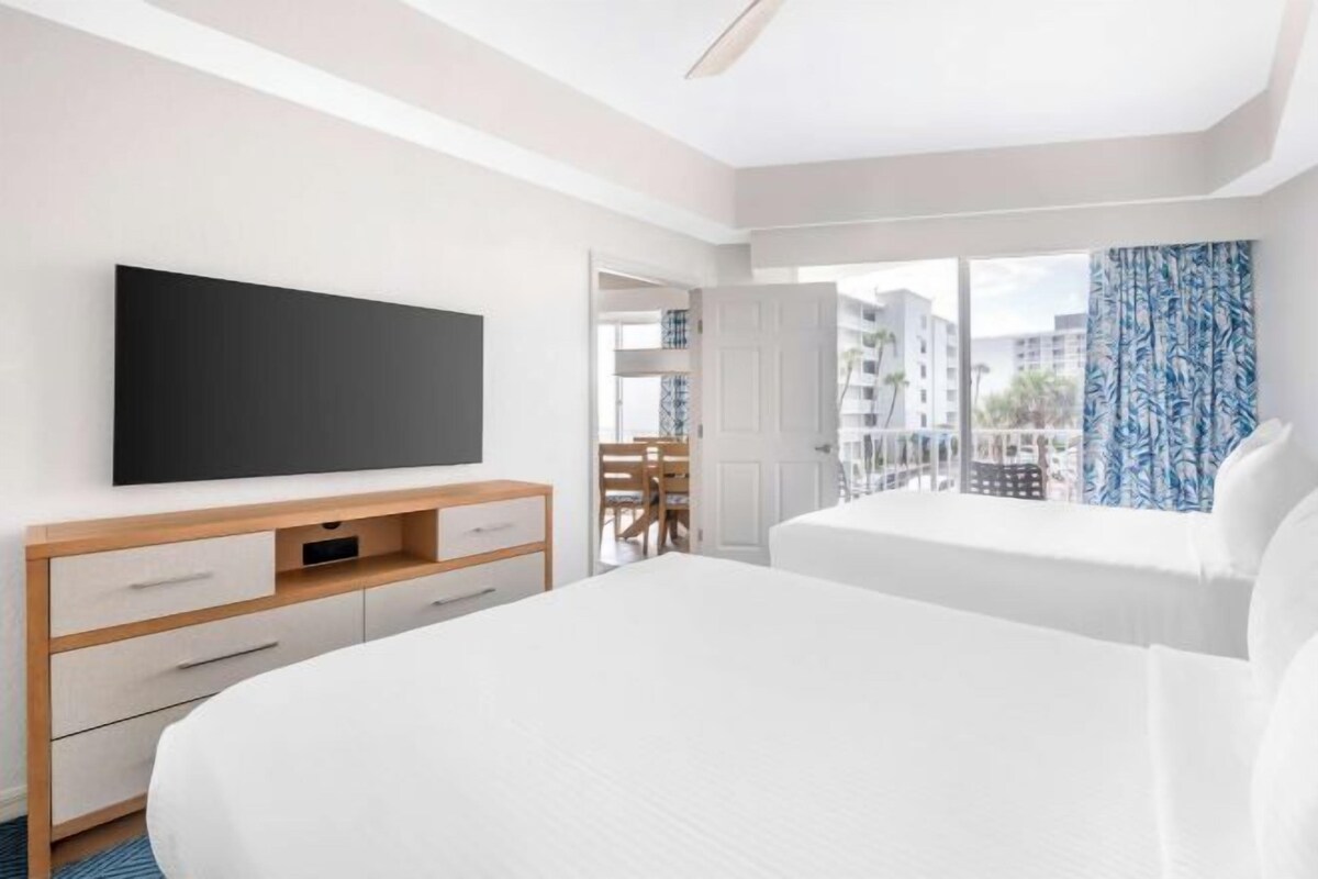 Quarto de hotel com cama, televisão, escrivaninha e varanda com vista.