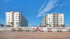 Un hôtel en bord de mer, avec plusieurs étages, des espaces de détente en plein air et des palmiers.