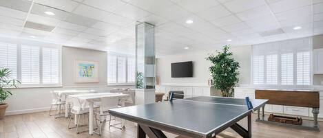 Una habitación amplia con mesa de ping pong, muebles blancos y ventanas grandes.
