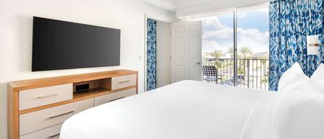 Habitación de hotel con una cama grande, un televisor de pantalla plana, un aparador de madera y un balcón con vista a la ciudad.