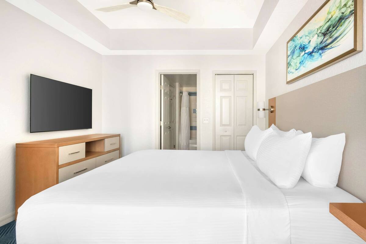 Ein Hotelzimmer mit einem großen Bett, einem Flachbildfernseher, einer Holzkommode und einem Deckenventilator.
