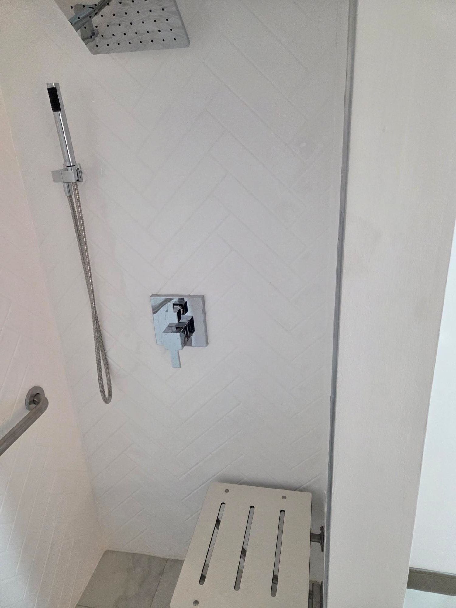 A shower area with a handheld showerhead, a wall-mounted control panel, and a metal grab bar.