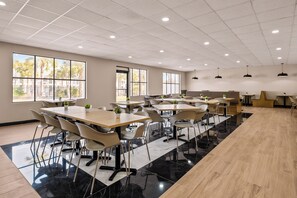 A spacious conference room with multiple tables and chairs, large windows with a view of palm trees, and a polished floor.