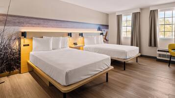 A hotel room with two beds, a desk, a chair, and a large window with curtains.