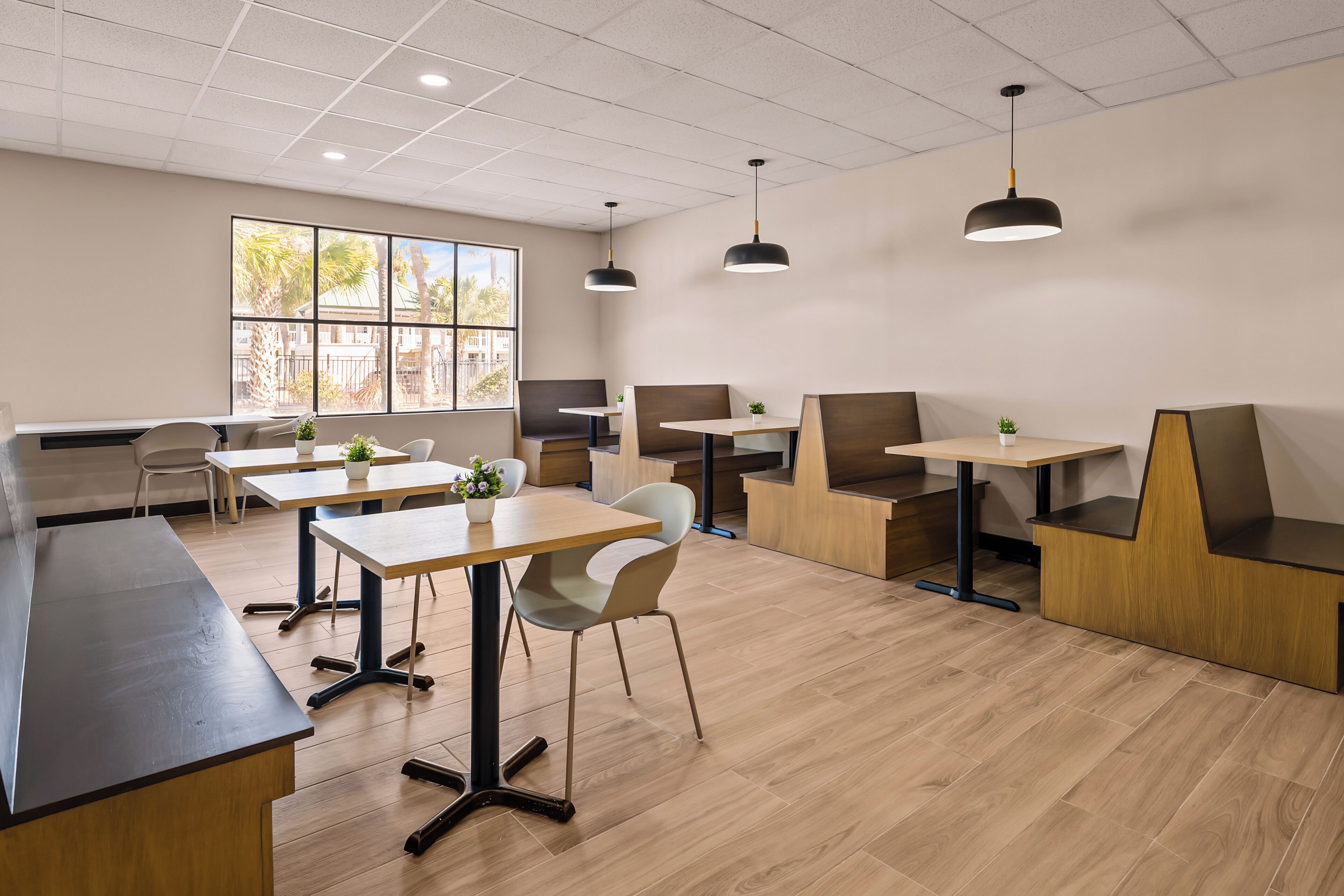 Un intérieur moderne avec de nombreuses tables et chaises, une grande fenêtre offrant une belle vue et des luminaires suspendus.