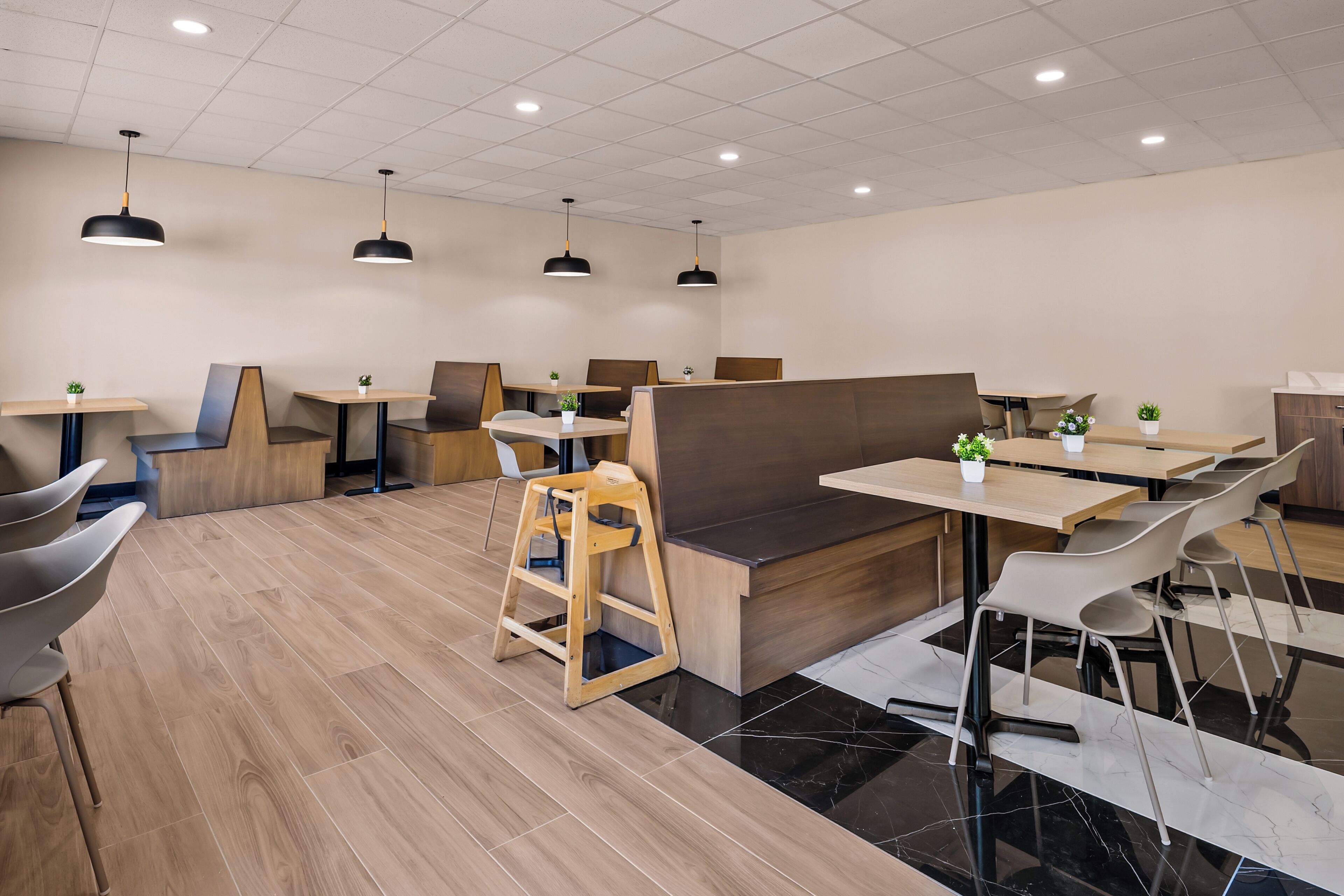 A modern restaurant interior with wooden flooring, black and white chairs, and pendant lighting.