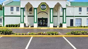 A B&B hotel with a central entrance, green-framed windows, and a parking lot in front.