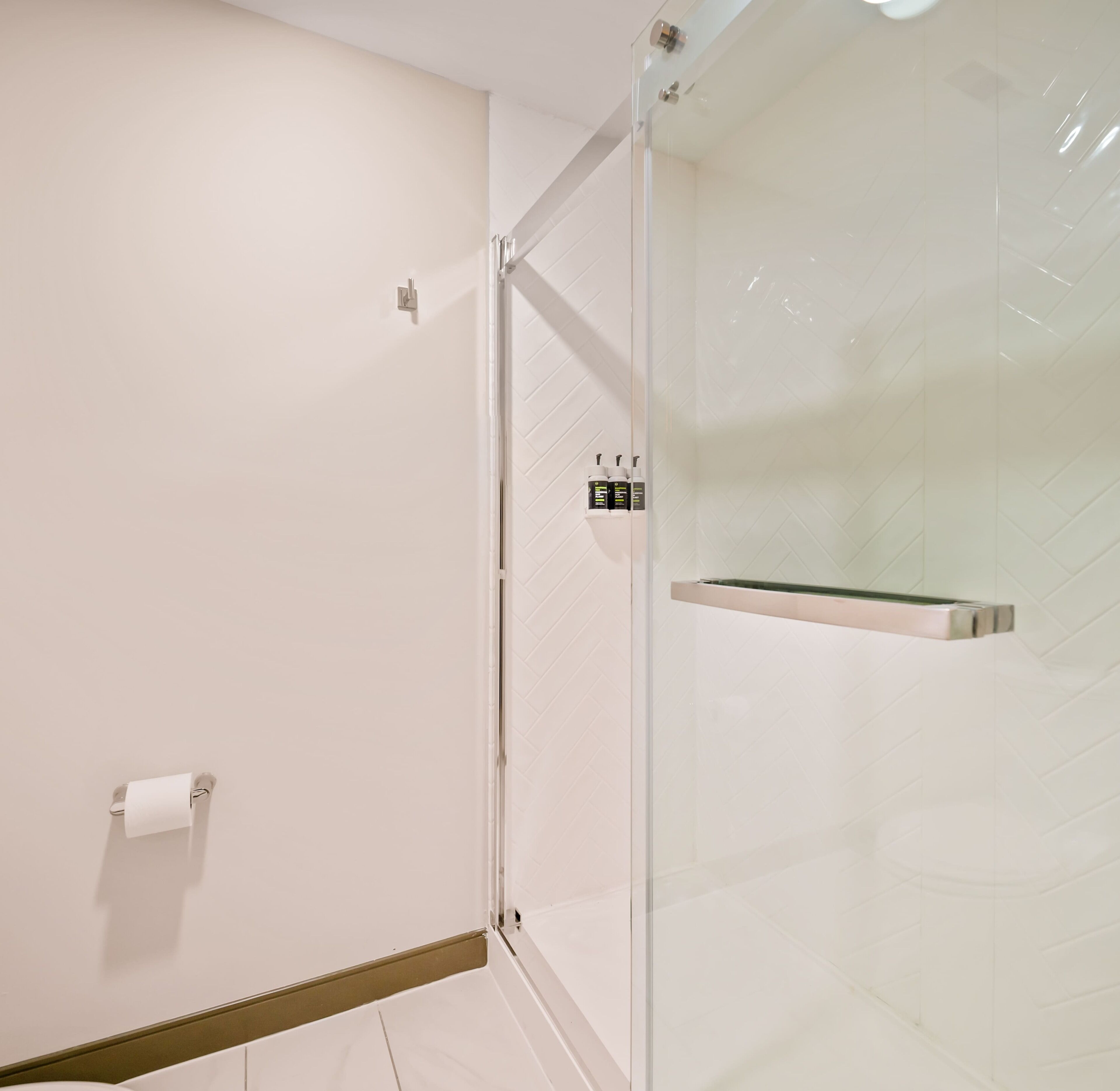 A modern bathroom with a glass shower enclosure, a toilet paper holder, and a towel rack.