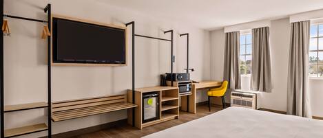 A hotel room with a bed, a desk with a computer, a TV, and a window with curtains.
