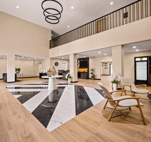Un hall d’entrée spacieux doté d’un sol central en marbre noir et blanc, d’un parquet, d’un lustre et d’un espace détente avec des fauteuils.