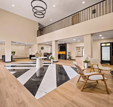 A spacious lobby with a central black and white marble floor, wooden flooring, a chandelier, and a seating area with chairs.