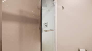 Um banheiro moderno com box de vidro, paredes revestidas de azulejos brancos e um rolo de papel higiênico à mostra.