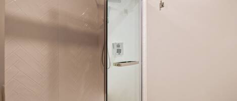 A modern bathroom with a glass shower enclosure, white tiled walls, and a visible toilet paper holder.