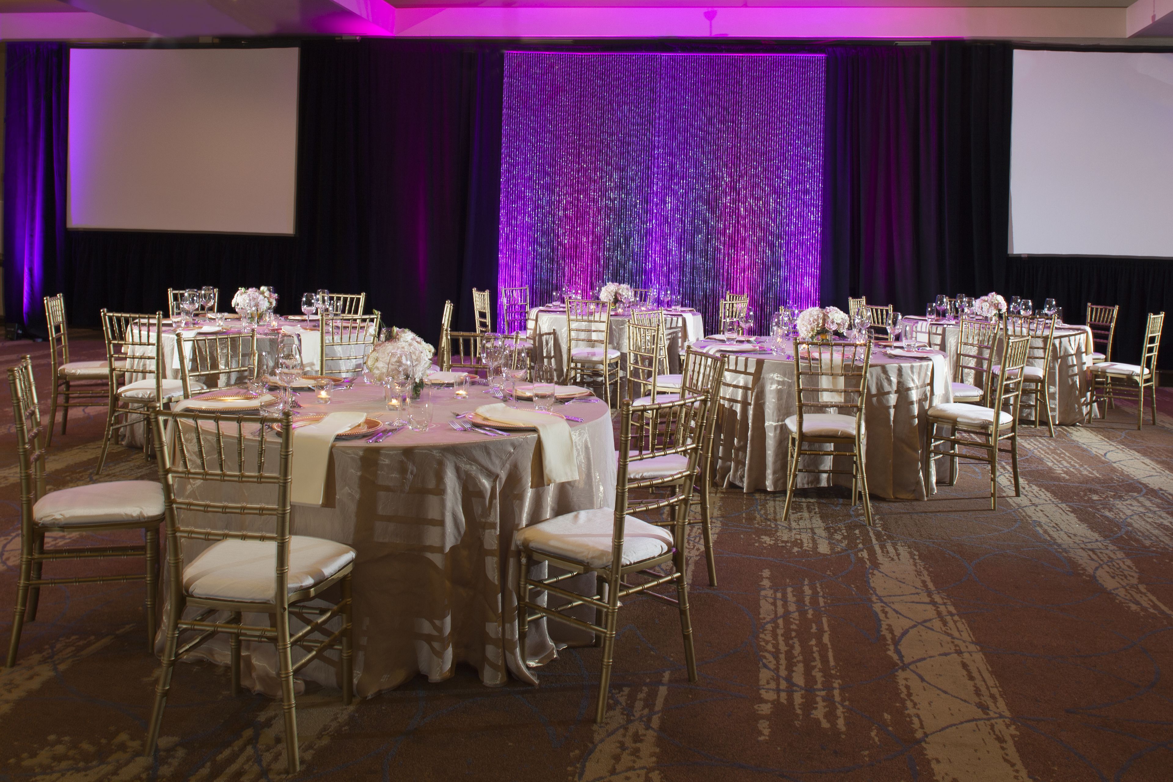 Un salón de banquetes con mesas redondas, sillas doradas y un fondo morado.