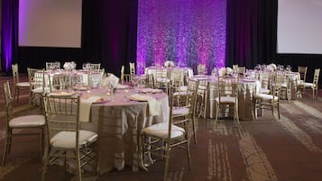 Un salón de banquetes con mesas redondas, sillas doradas y un fondo morado.