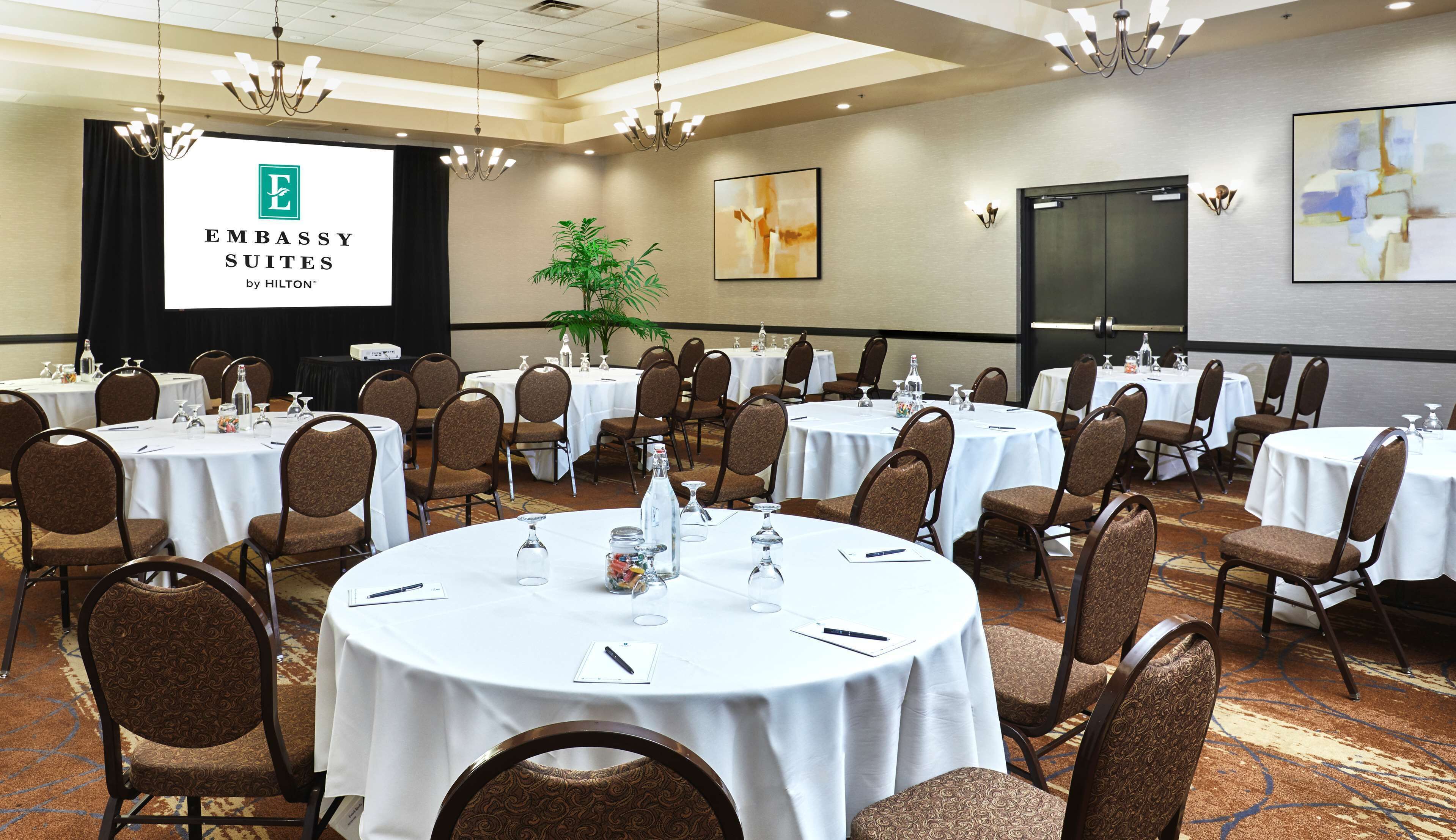 A conference room with round tables, chairs, and a presentation screen displaying 'EMBASSY SUITES by HILTON'.