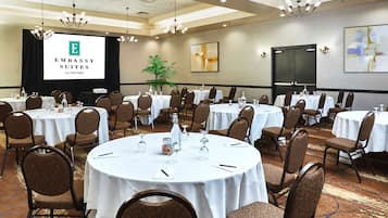 A conference room with round tables, chairs, and a presentation screen displaying 'EMBASSY SUITES by HILTON'.