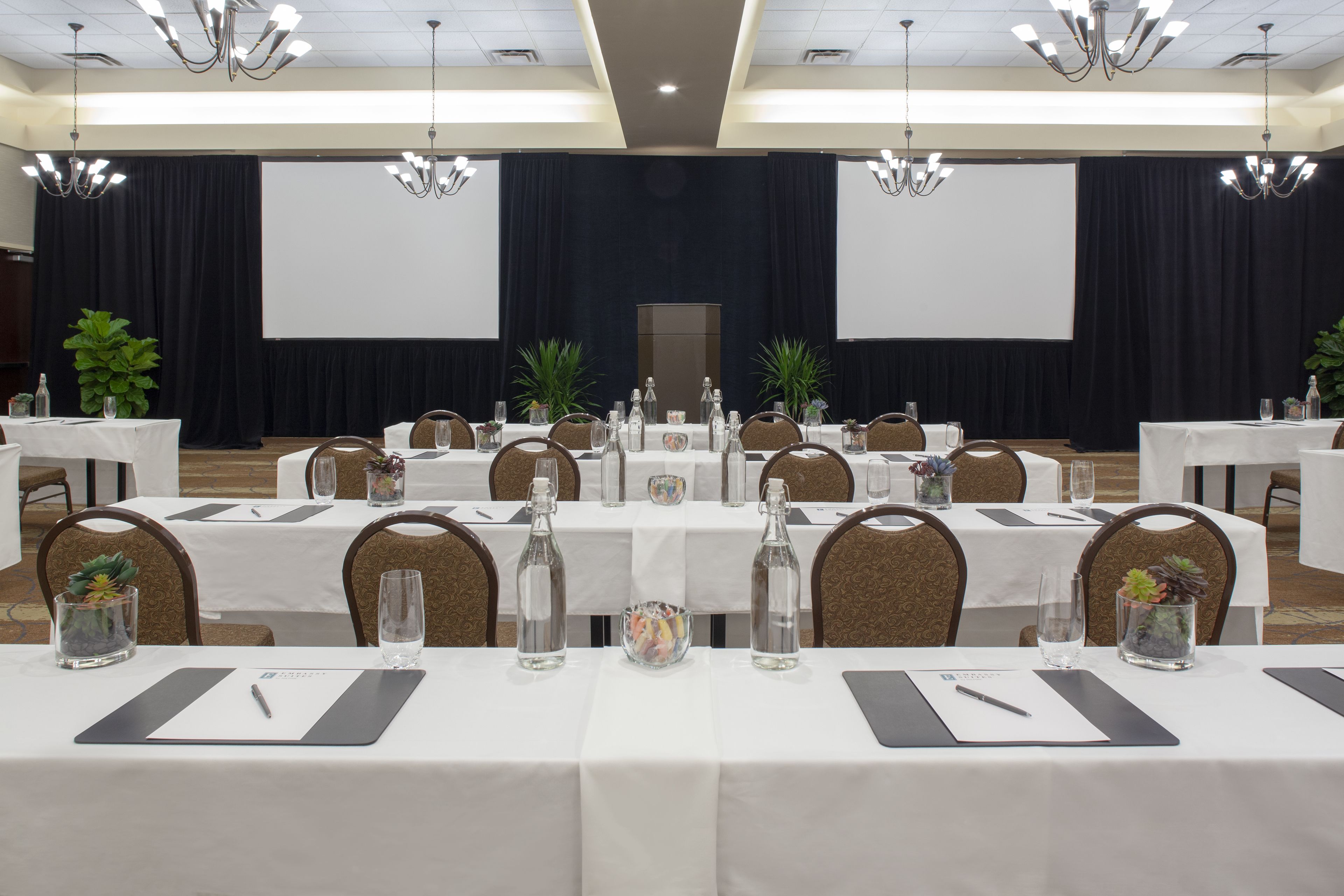 A conference room with multiple tables, chairs, and a stage with a screen.