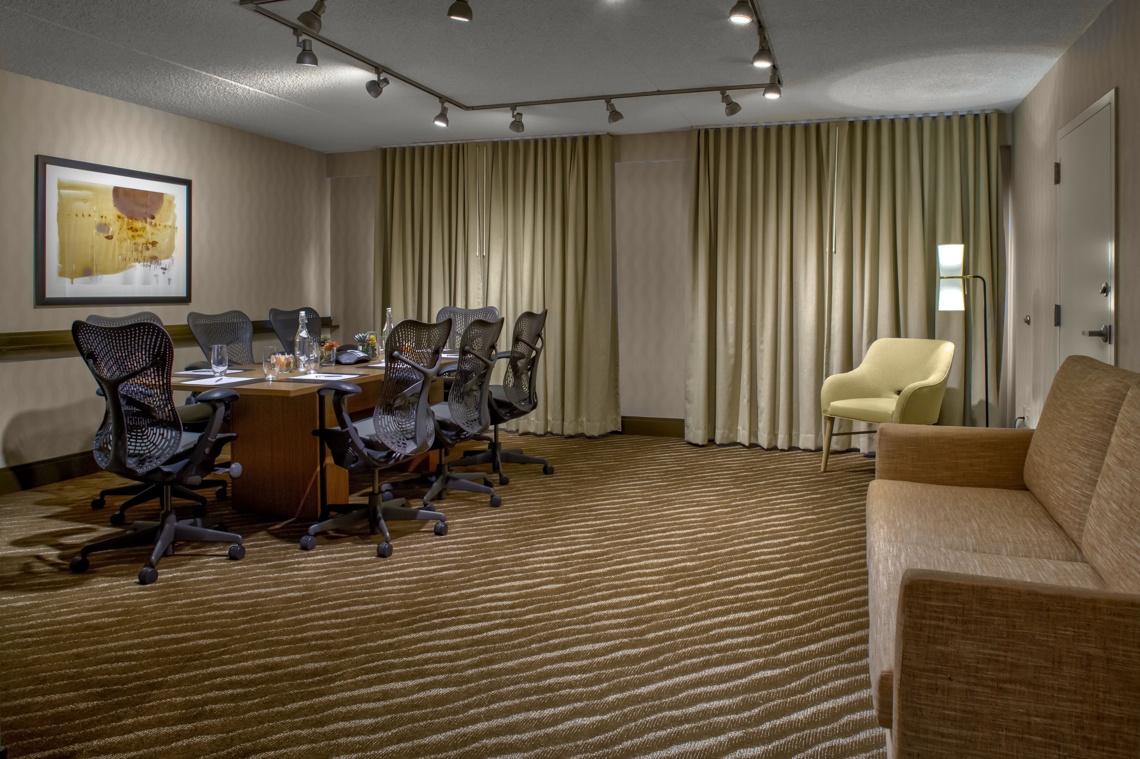 A conference room with a long table, multiple chairs, a sofa, and a large window with curtains.