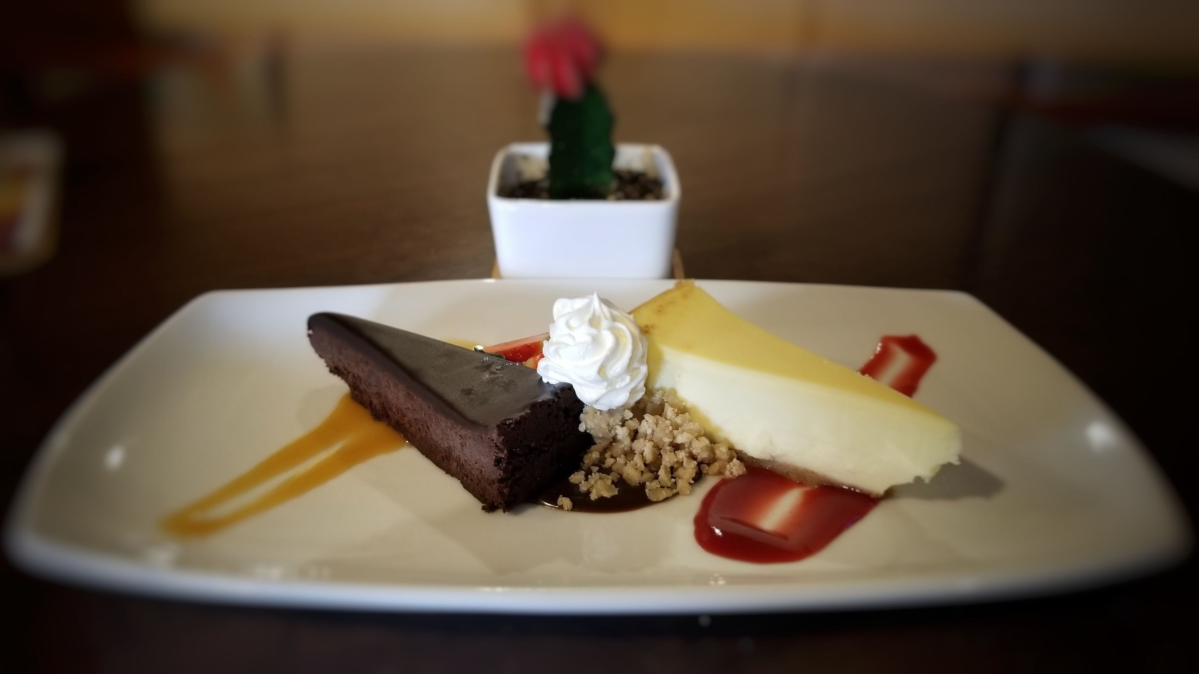 A dessert plate with a chocolate cake, a scoop of ice cream, and a piece of cheesecake, accompanied by a small potted plant.