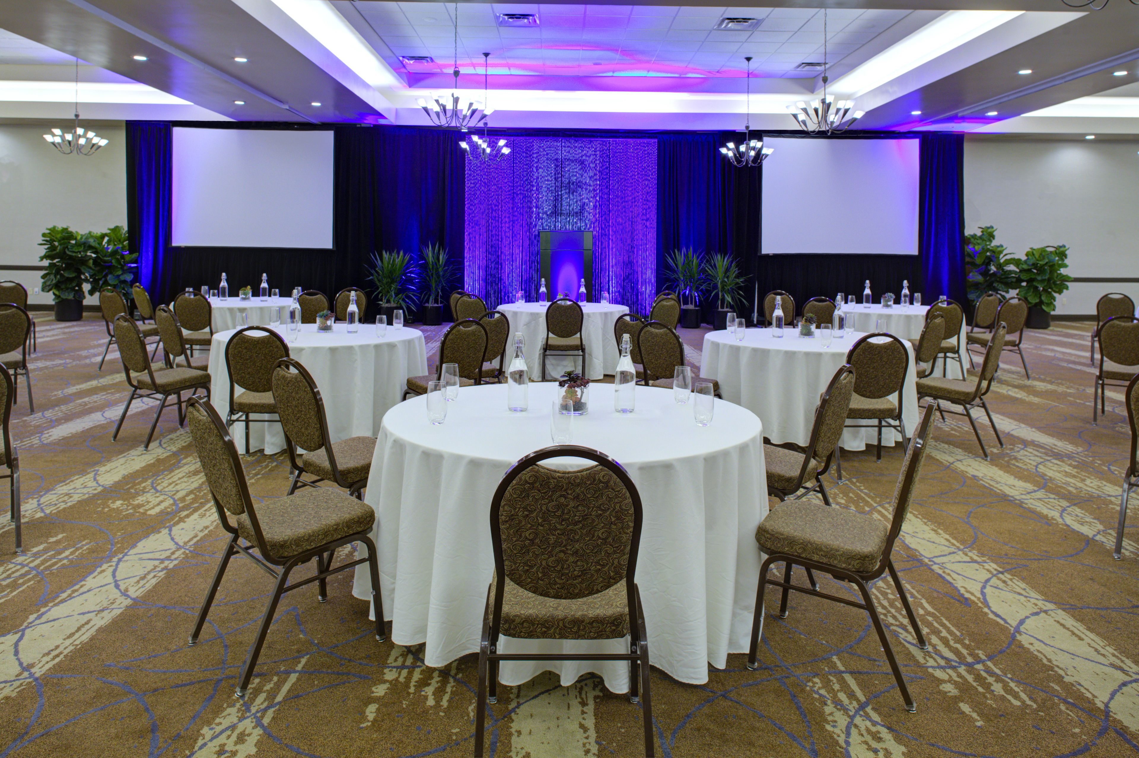 A conference room with round tables, chairs, and a stage with a blue curtain backdrop.