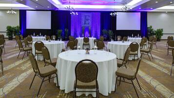 A conference room with round tables, chairs, and a stage with a blue curtain backdrop.