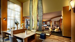 Eine großzügige Hotelhalle mit Empfangsschalter, Sitzbereichen und Blick auf den Speise- und Küchenbereich.