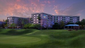 Ein mehrstöckiges Hotel mit flachem Dach und Balkonen, umgeben von gepflegtem Rasen und Bäumen.