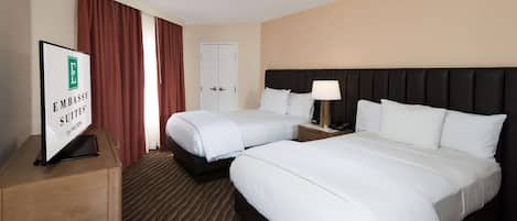 Habitación de hotel con dos camas, un escritorio, una lámpara y un cartel que indica que es un Embassy Suites by Hilton.