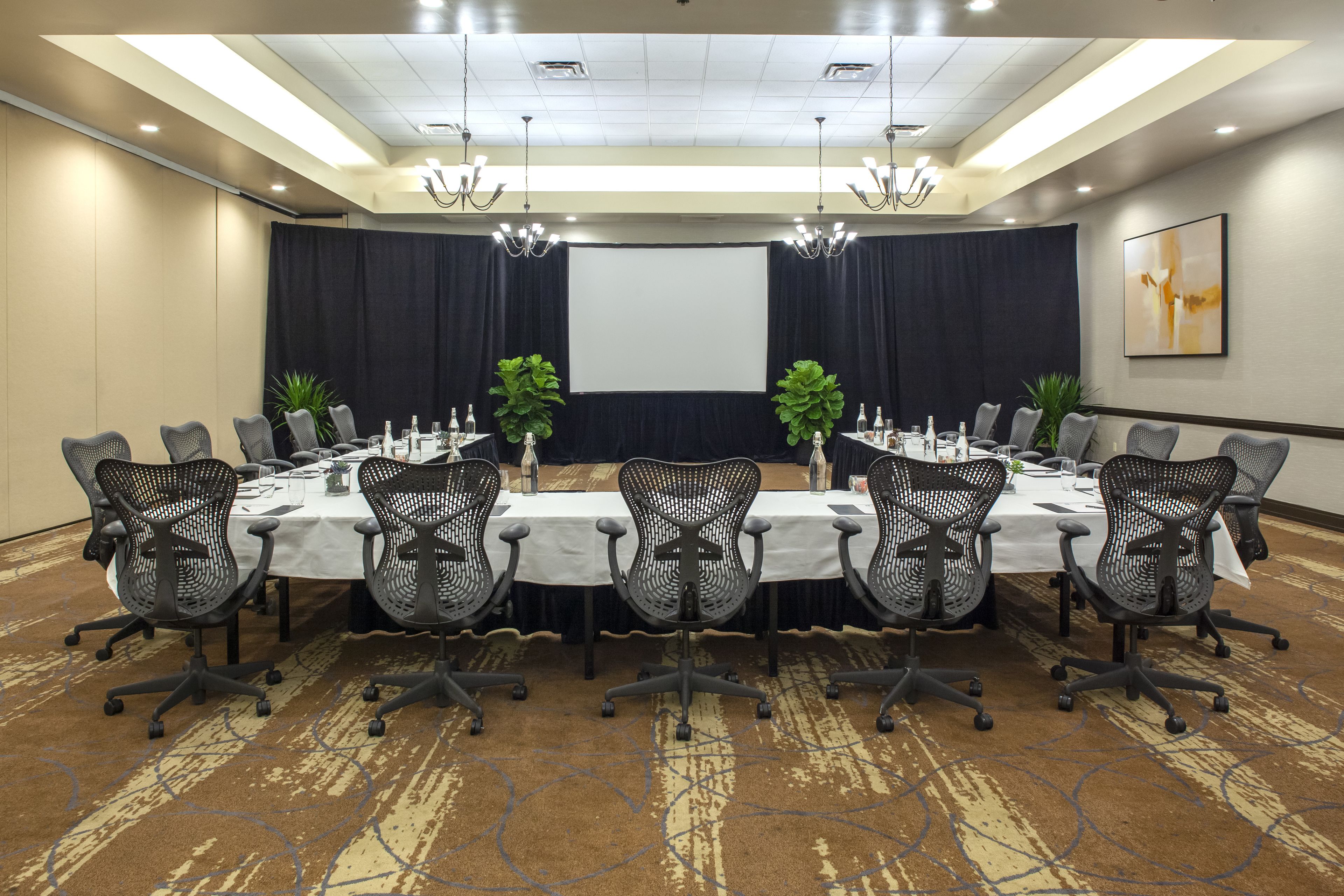 A conference room with a long table, chairs, a projector screen, and a carpeted floor.