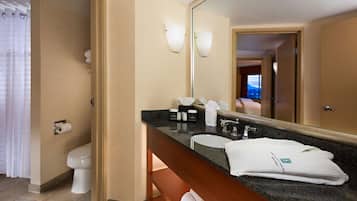 Een moderne badkamer met een grote spiegel, een wastafel en een toilet. Handdoeken en toiletartikelen liggen op het aanrecht.