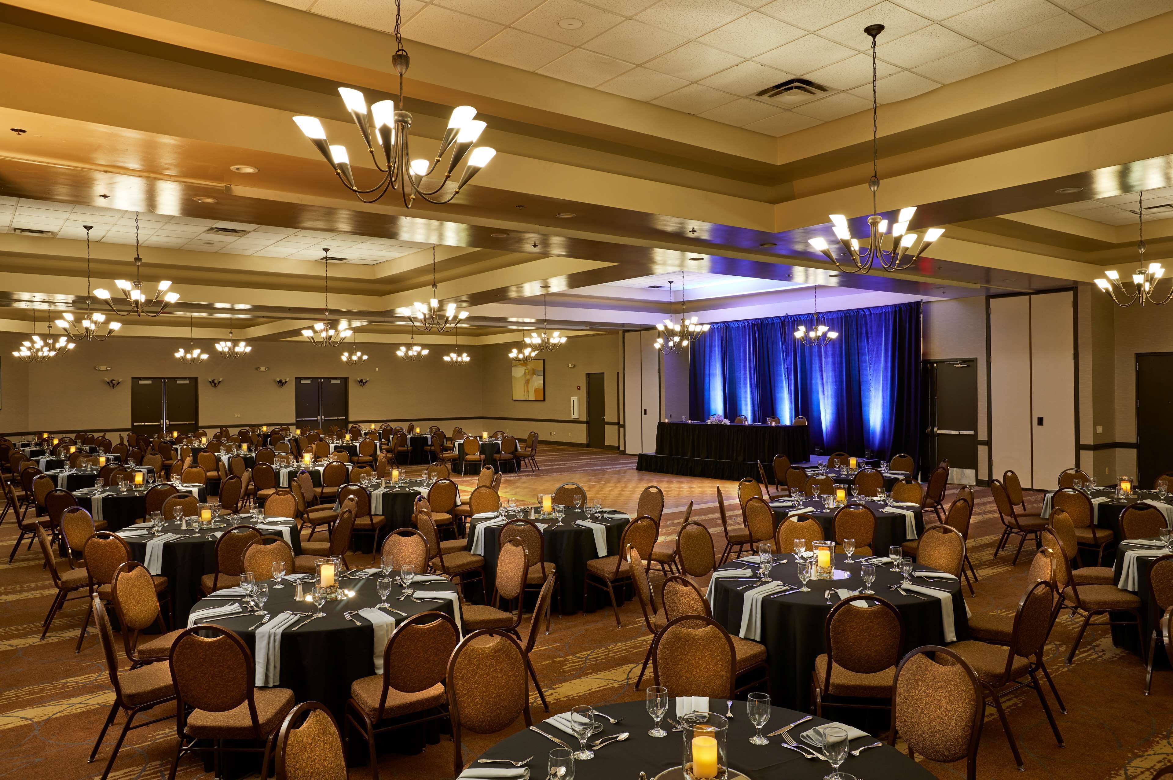 A large banquet hall with multiple round tables set for dining, arranged in rows.