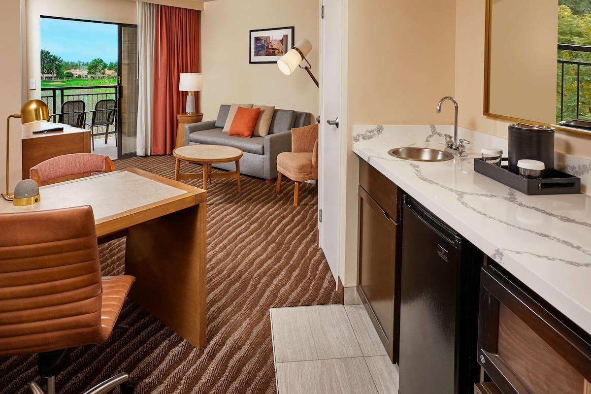 Quarto de hotel com área de refeições, sofá, cozinha com pia e vista para o exterior.