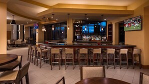 Eine Bar mit verschiedenen Sitzgelegenheiten, einer Bar und einem Fernsehbildschirm, der Sport zeigt.