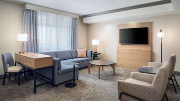 Una habitación de hotel moderna con un sofá, un escritorio, una silla, una mesa redonda y un televisor montado en la pared.