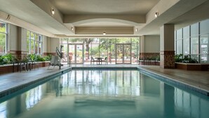 Ein Innenpool mit großen Glaswänden, gefliestem Boden und einigen Liegestühlen und Tischen.